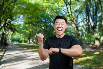 Male asian athlete on a morning run rejoices at the achieved result, smiles.