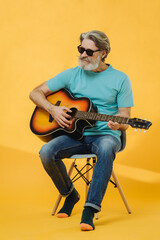 Studio portrait of an elderly, gray-haired man in sunglasses playing the guitar.