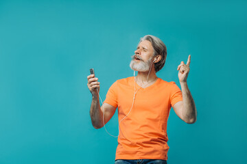 Gray-haired senior man in wired headphones with a phone posing on a blue background. Studio shooting.