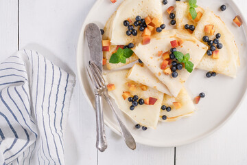 Pancakes with blueberries, peach and mint on a plate. White wooden table. Light background. Serving a rustic table with yellow flowers and a yellow drink