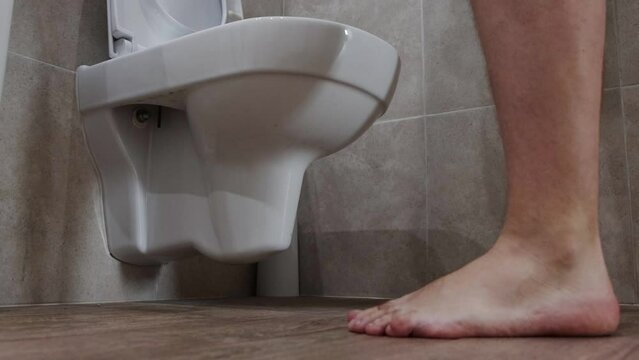 The man lifts the lid of the toilet bowl and cannot urinate in the toilet. Problems with urination in men, close-up