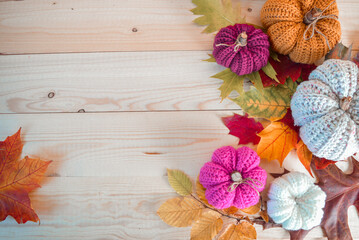 colorful handmade crochet pumpkins on light wooden ground, woolen balls and autumn leaves with space for text