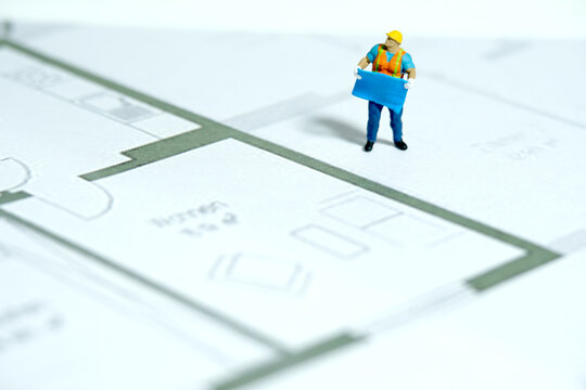 Miniature people toy figure photography. Architectural sketching process concept. A construction worker holding blueprint standing above building sketch draw