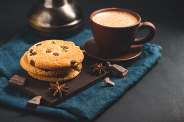Crispy oatmeal cookies with raisins, coffee cup and turkish coffee pot, chocolate chunks on a dark background