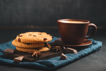 Crispy oatmeal cookies with raisins, coffee cup and chocolate chunks on a dark background