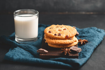 Crispy oatmeal cookies with raisins and glass with milk on wooden board, dark background