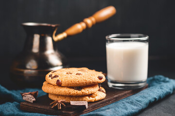 Crispy oatmeal cookies with raisins, glass with milk and turkish coffee pot on a dark background