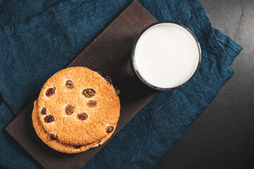 Crispy oatmeal cookies with raisins and glass with milk on wooden board, top view