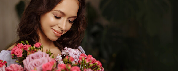 Banner portrait of a beautiful young brunette woman in a purple dress. She is holding a vintage vase with a large spring bouquet of pink natural flowers.