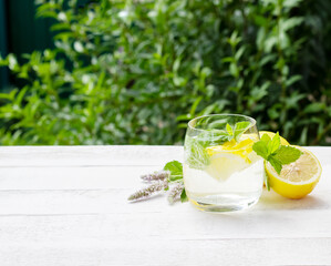 Homemade lemonade with lemon, mint and ice cubes in a glass on the white wood table with lemons and mint flowers