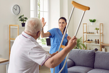 It's getting dangerous in here. Angry, aggressive, bad tempered senior patient fighting with medical worker. Old man becomes uncontrollable and threatens scared nurse or volunteer medic with crutch - obrazy, fototapety, plakaty