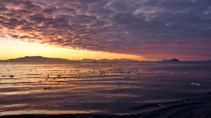 Fototapeta na wymiar Colorful sunset over mountains and a field of floating icebergs at Cierva Cove, Antarctica