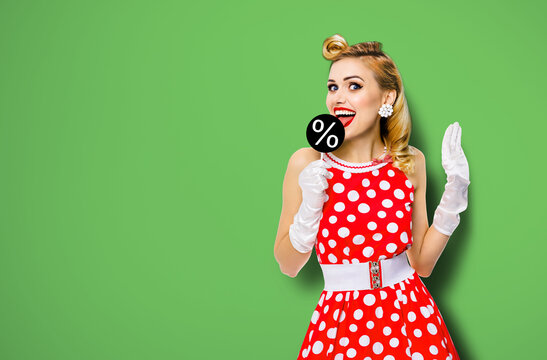 Very tasty discounts, rebates, deals concept image. Cheerful beautiful woman licking signboard with % sign, dressed in pinup red dress, isolated over green background. Black Friday sales ad.