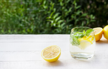 Homemade lemonade with lemon, mint and ice cubes in a glass on the white wood table with lemons.