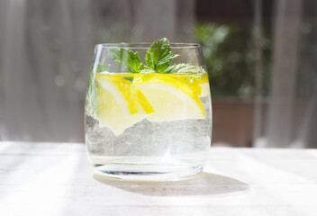 Close-up of homemade lemonade with lemon, mint and ice cubes in a glass on white wood table