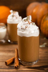 Pumpkin spice latte in glass mug with cinnamon, nutmeg, pumpkin seeds and whipped cream on brown texture wood. A glass of autumn coffee with pumpkin. A warming drink. Autumn concept.