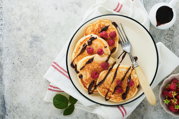 American pancakes. Pancakes with fresh raspberry with chocolate glaze or toppings in gray bowl on light gray table background. Homemade classic american pancakes. Page for magazine concept. Top view.