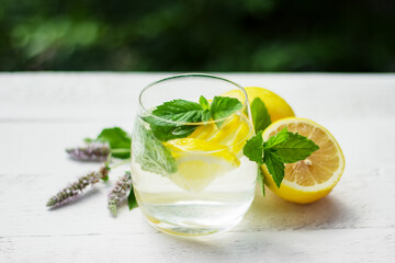 Close-up of homemade lemonade with lemon, mint and ice cubes on the white wood table with lemons and mint flowers