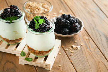 Yogurt with granola, blackberry berry fruits and muesli served in glass jar on wooden background....