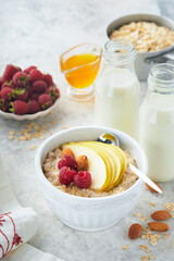 Oatmeal. Bowl of oatmeal porridge with raspberry, pear and honey on gray concrete old table background. Hot and healthy food for Breakfast, top view, flat lay