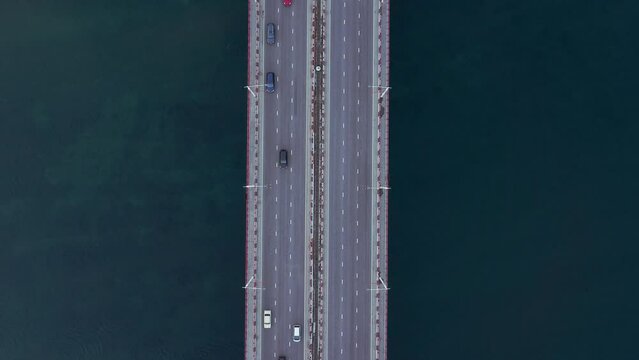 4k Top view of cars drive over bridge along waters in open air irrl. Above view of transport driving on asphalt highway surrounded by blue waters outdoors. Operator launches drone and takes pictures
