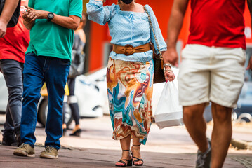 Brazilian woman wearing blue blouse and colorful skirt carrying a white shopping bag walking among male pedestrians at Savassi, Belo Horizonte, Brazil.