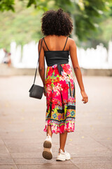Back view of young black Brazilian woman wearing a black top and colorful pants walking towards the fountain at Savassi, Belo Horizonte, Brazil.
