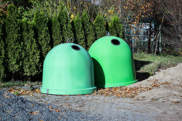 Two green spherical garbage containers standing on pathway with gravel and sand in front of fir trees