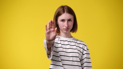 4k video of young female showing stop sign isolated over yellow background.