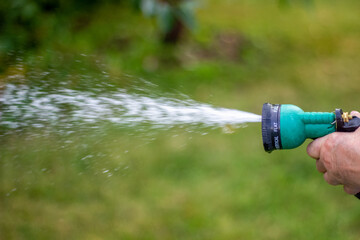 Female hand holding a garden hose, adjustable shower, spray. Summer garden watering.