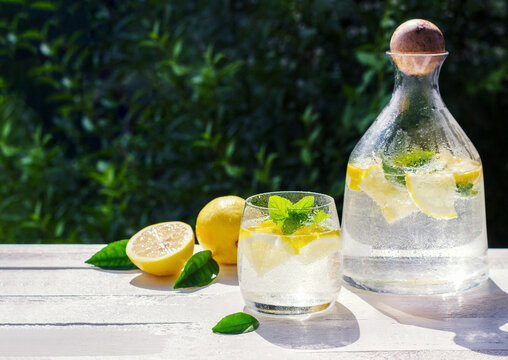 Homemade lemonade with lemon, mint and ice cubes in a glass pitcher on the white wood table with lemons.