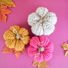 yellow, white and pink handmade crochet pumpkin with autumn leaves on pink ground