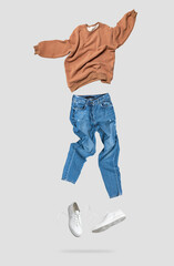 Fashionable flying brown cotton stylish sweatshirt, blue jeans, leather sneakers isolated on gray...