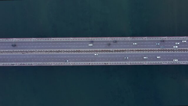 4k Top view of transport ride on road bridge outdoors irrl. Aerial of cars driving along asphalt highway over blue waters of sea or river outdoors in summer. Amazing drone picture of vehicles moving