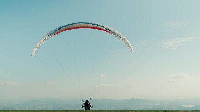 Professional paraglider with parachute run and take off from mountain top. Launch into air on a clear sky day. Adrenaline extreme sport into air