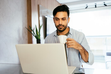 Man working at home using laptop drinking coffee