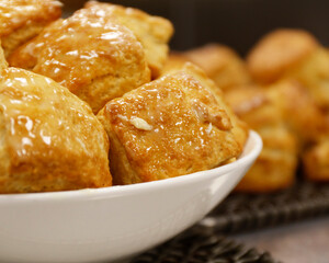fresh baked biscuits lightly drizzled with butter displayed in  a white bowl 