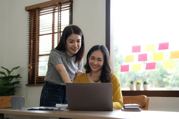 Two young Asian business woman talk, consult, discuss working with new startup project idea presentation analyze plan marketing and investment in the office.