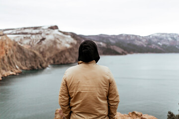 a young man reflects and is sad near a beautiful landscape, mountains and sea