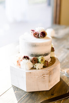 Elegant little wedding cake with white icing and roses (maroon, white, fall colors) on a rustic table.  
