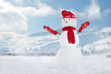 Snowman wearing red hat, gloves and scarf against snowy mountains landscape