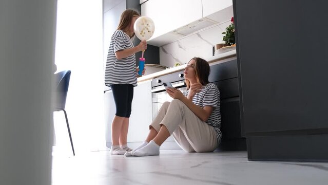 A young woman is looking at the phone while sitting on the floor in a modern kitchen.