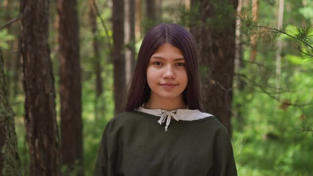 Dark-haired girl in medieval dress smiles in woods, close-up
