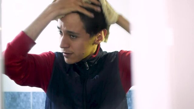 Joven hombre caucasico y delgado secando su cabello con una toalla frente a un espejo en un ba&ntilde;o 