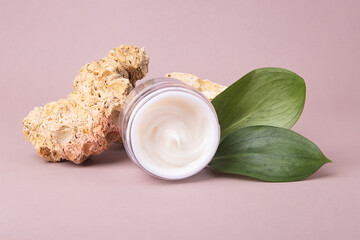 Open cosmetics container with white cream and glossy green leafs on background,eco friendly concept.