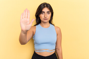 Young Indian woman isolated on yellow background standing with outstretched hand showing stop sign,...