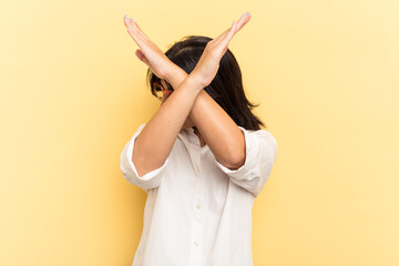 Young Indian woman isolated on yellow background keeping two arms crossed, denial concept.