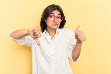 Young Indian woman isolated on yellow background showing thumbs up and thumbs down, difficult choose concept