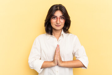 Young Indian woman isolated on yellow background praying, showing devotion, religious person...
