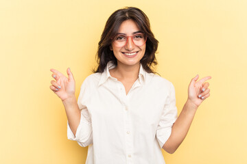 Young Indian woman isolated on yellow background pointing to different copy spaces, choosing one of them, showing with finger.